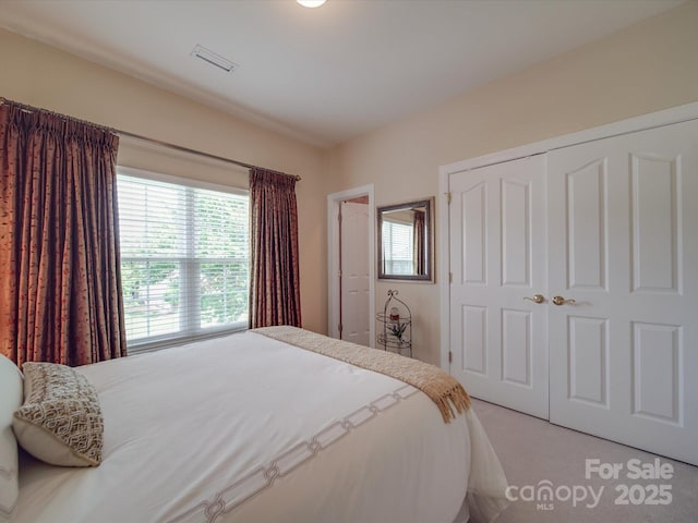 bedroom with a closet, multiple windows, light colored carpet, and visible vents