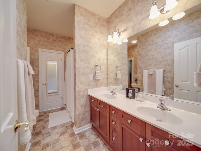 full bathroom with a sink, stone finish floor, baseboards, and double vanity