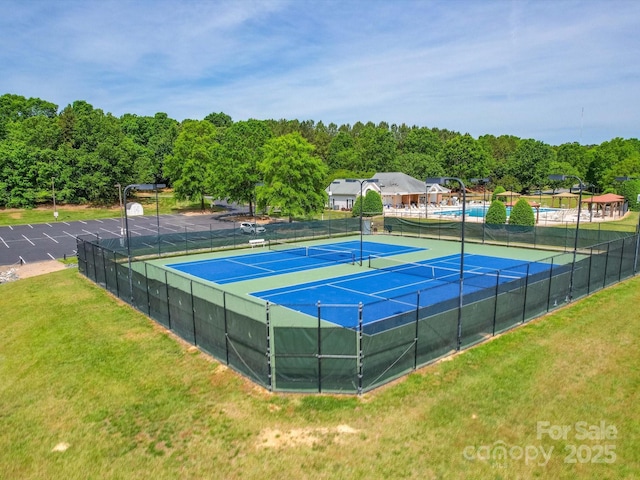 view of tennis court featuring fence and a yard