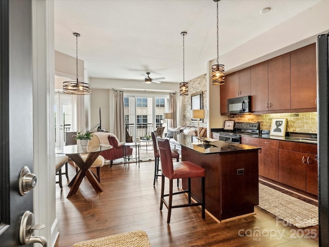 kitchen featuring black appliances, dark countertops, dark wood finished floors, a breakfast bar area, and a ceiling fan