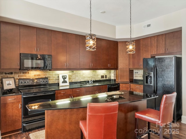 kitchen featuring black appliances, a sink, a breakfast bar area, backsplash, and a center island