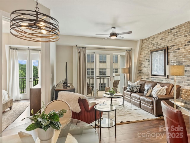 living room featuring a ceiling fan, wood finished floors, brick wall, and french doors