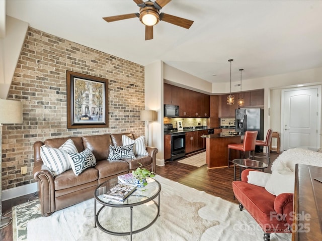 living room featuring brick wall, dark wood-style flooring, baseboards, and ceiling fan