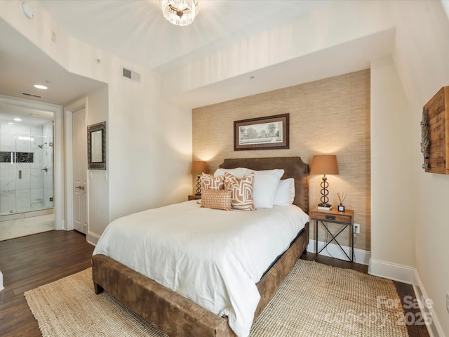 bedroom featuring ensuite bathroom, baseboards, visible vents, and wood finished floors