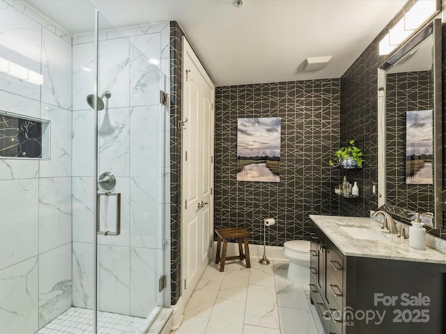 bathroom with toilet, a marble finish shower, tile walls, marble finish floor, and vanity