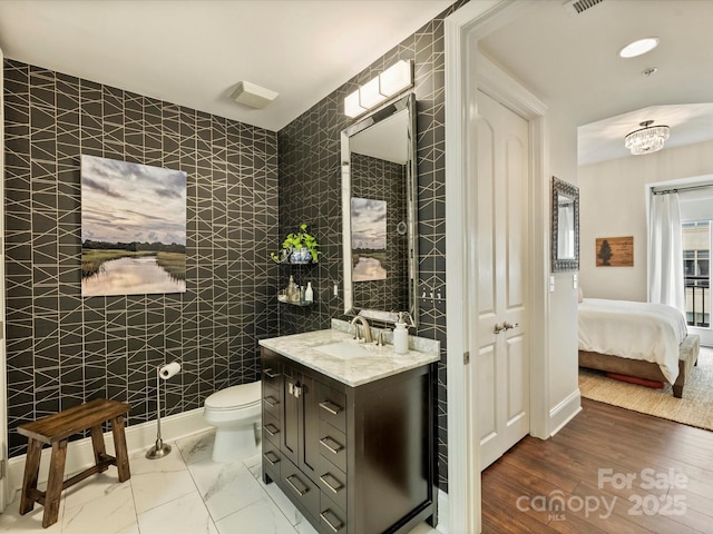 ensuite bathroom with connected bathroom, toilet, an inviting chandelier, tile walls, and vanity