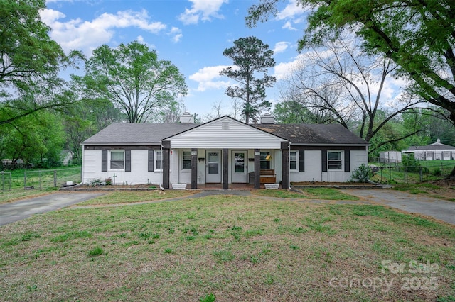 view of front facade with driveway, a chimney, covered porch, a front yard, and fence