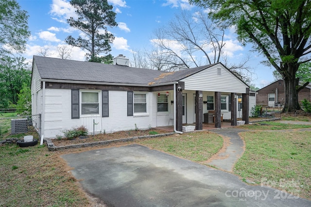view of front of house with a front yard, a shingled roof, a chimney, covered porch, and brick siding