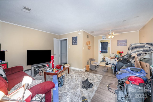 living area with wood finished floors, baseboards, visible vents, a ceiling fan, and crown molding