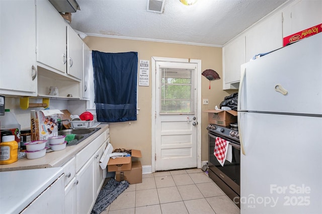 kitchen featuring white cabinets, visible vents, light countertops, freestanding refrigerator, and electric stove