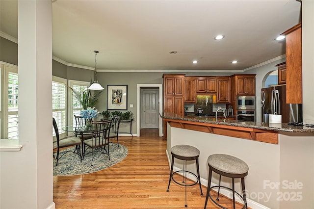 11232 Tradition View Dr, Charlotte, NC 28269 - kitchen featuring stainless steel appliances, crown molding, a breakfast bar area, light wood finished floors, and dark stone countertops