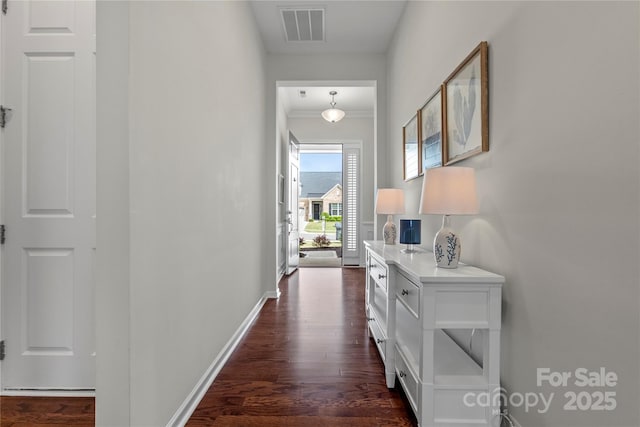 hall featuring dark wood-style flooring, baseboards, visible vents, and ornamental molding