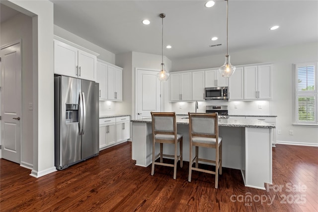 kitchen with white cabinets, appliances with stainless steel finishes, a center island with sink, and dark wood-type flooring