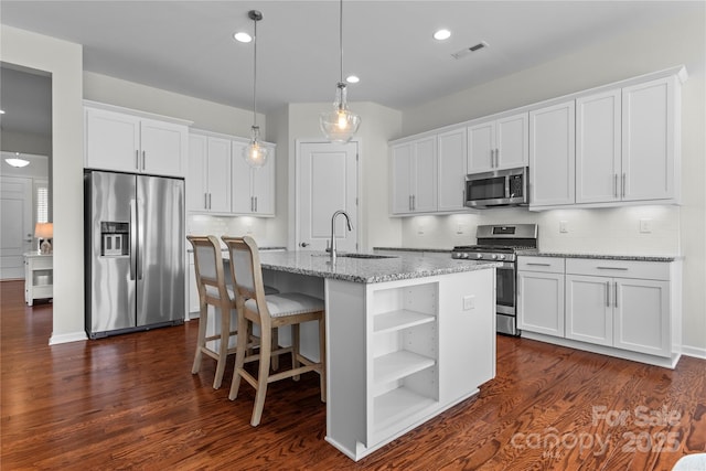 kitchen with dark wood-style flooring, appliances with stainless steel finishes, a sink, white cabinetry, and backsplash