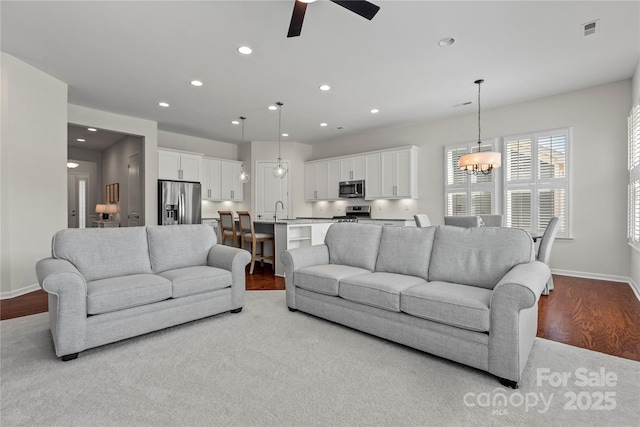 living room with visible vents, wood finished floors, baseboards, ceiling fan with notable chandelier, and recessed lighting