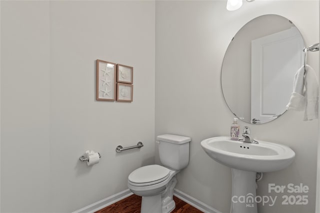 half bathroom with baseboards, toilet, and wood finished floors