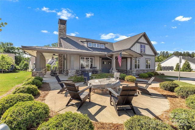 back of house with board and batten siding, a chimney, an outdoor fire pit, a patio, and stone siding