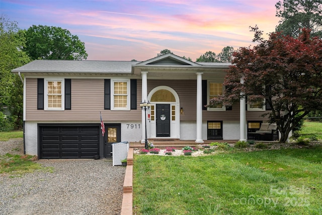 bi-level home with a garage, brick siding, driveway, and a yard
