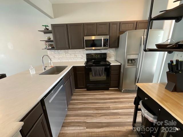 kitchen with appliances with stainless steel finishes, light countertops, open shelves, and a sink