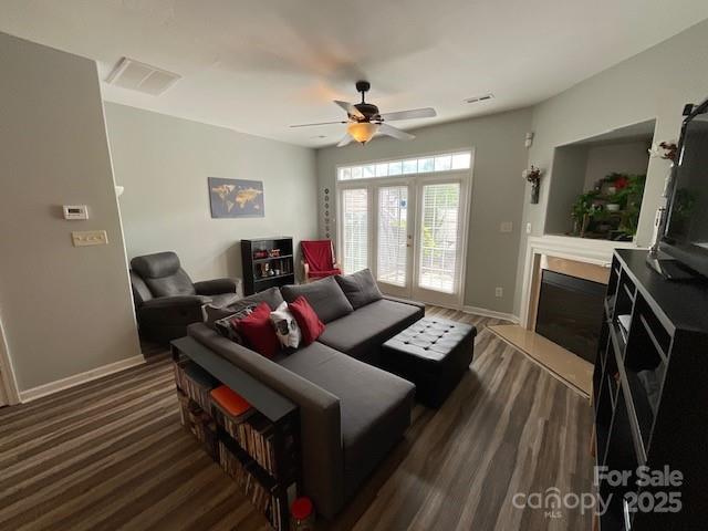 living area with visible vents, ceiling fan, dark wood-style floors, baseboards, and a glass covered fireplace