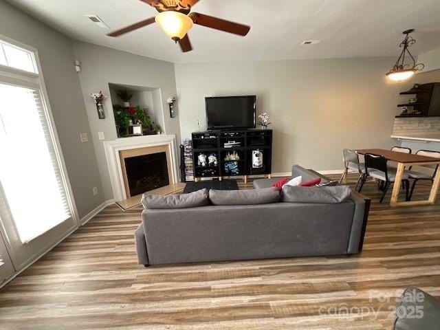 living area featuring light wood-style floors, a fireplace with raised hearth, baseboards, visible vents, and a ceiling fan