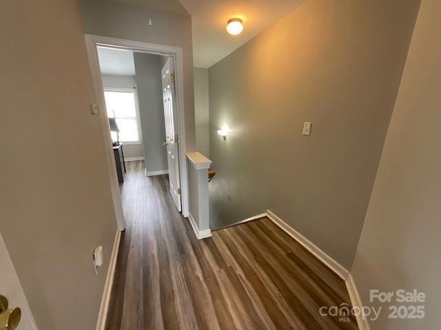 corridor featuring an upstairs landing, baseboards, and dark wood finished floors
