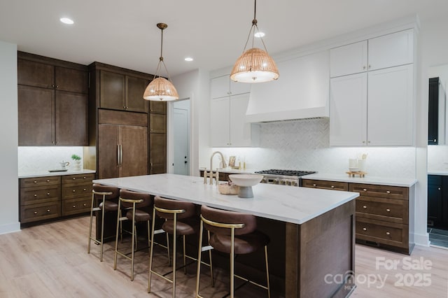 1807 Arnold Dr, Charlotte, NC 28205 - kitchen featuring light wood finished floors, tasteful backsplash, white cabinetry, a breakfast bar, and light stone countertops