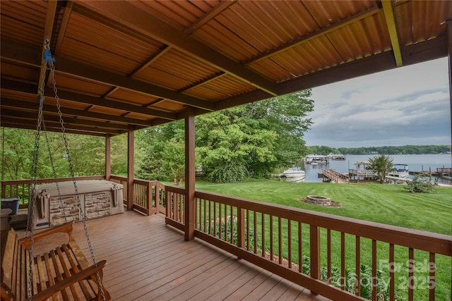wooden terrace with a lawn, a water view, a fire pit, and a hot tub