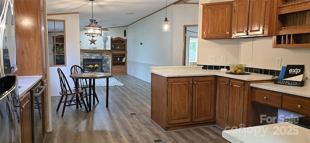 kitchen featuring brown cabinetry, a stone fireplace, wood finished floors, and light countertops