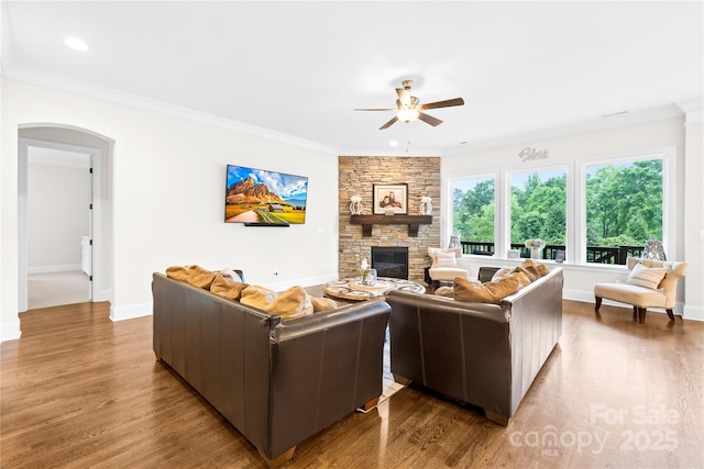 living room with crown molding, a stone fireplace, a ceiling fan, and wood finished floors