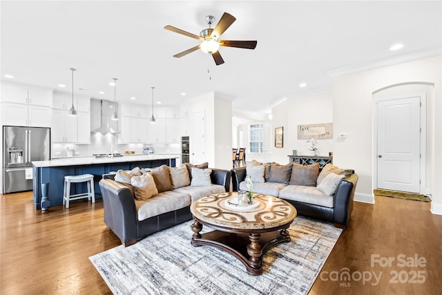 living room with wood finished floors, ornamental molding, recessed lighting, a ceiling fan, and baseboards
