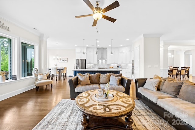 living area featuring wood finished floors, ceiling fan with notable chandelier, decorative columns, crown molding, and recessed lighting