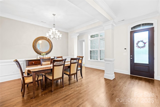 dining space with a chandelier, crown molding, decorative columns, and wood finished floors