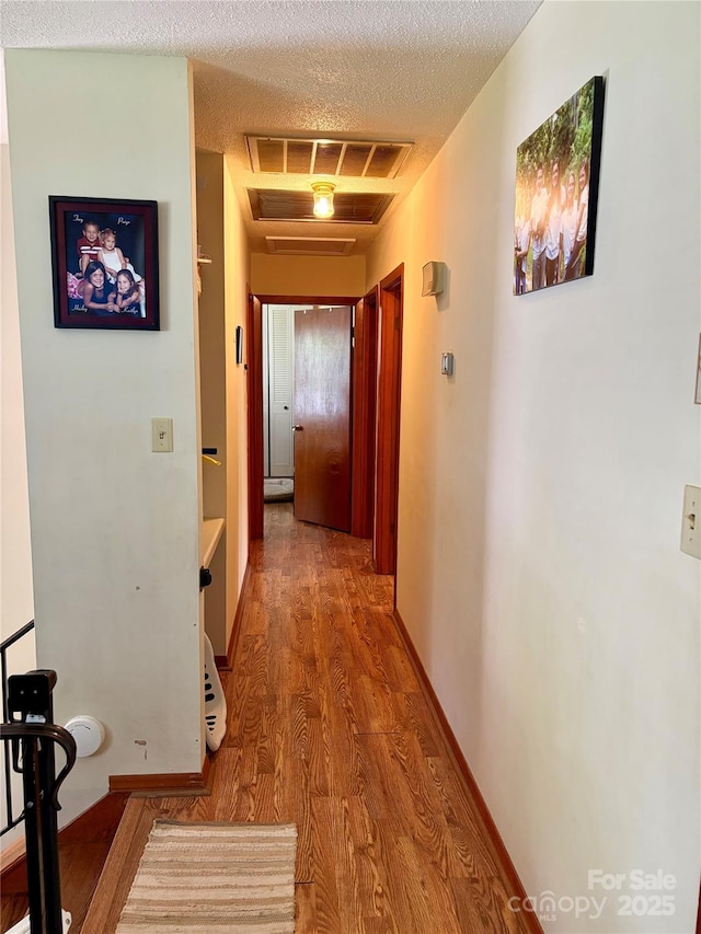 hallway with wood finished floors, attic access, baseboards, visible vents, and a textured ceiling