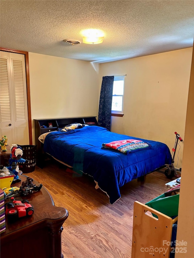 bedroom with a textured ceiling, visible vents, and wood finished floors