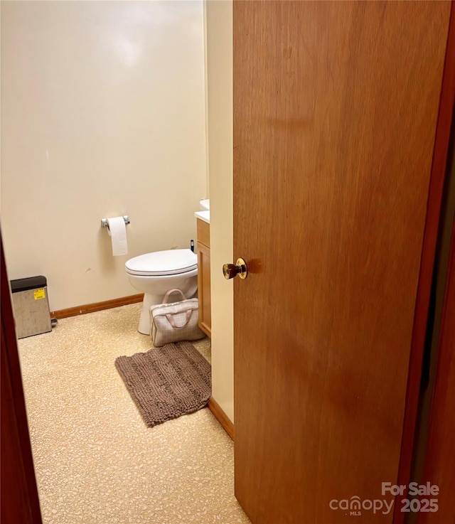 half bathroom featuring baseboards, toilet, and vanity