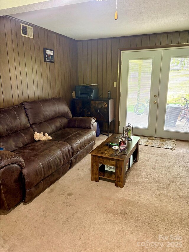 carpeted living area featuring visible vents, wooden walls, and french doors