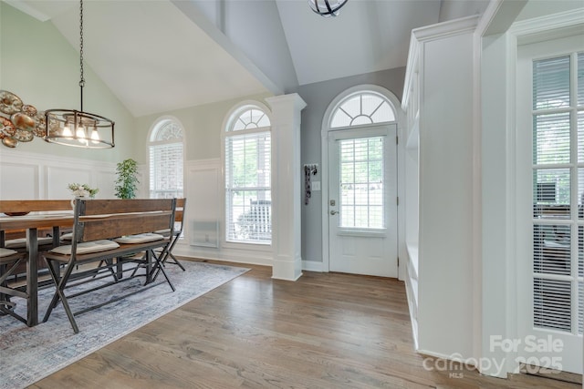 foyer entrance with decorative columns, wood finished floors, high vaulted ceiling, a notable chandelier, and a decorative wall