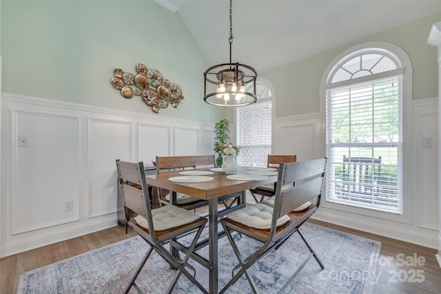 dining room with vaulted ceiling, a wainscoted wall, an inviting chandelier, a decorative wall, and light wood-style flooring