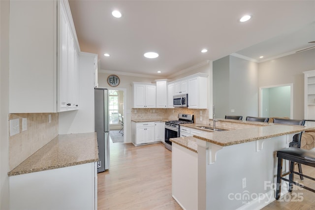 kitchen featuring a kitchen breakfast bar, appliances with stainless steel finishes, ornamental molding, and a sink