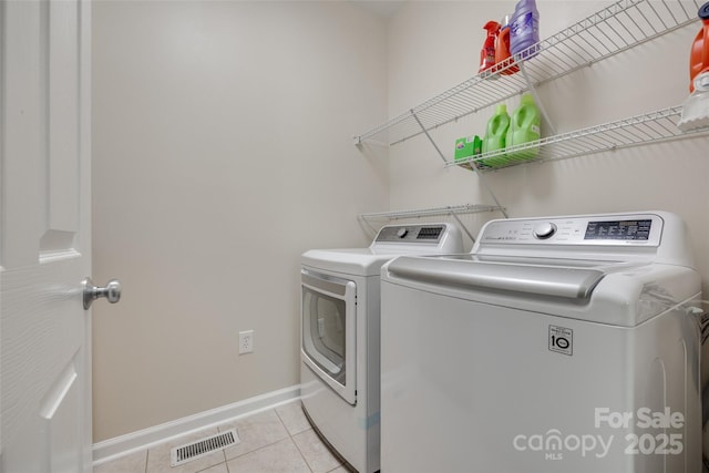 laundry area with laundry area, visible vents, baseboards, washing machine and clothes dryer, and light tile patterned floors