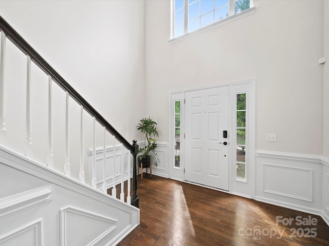 entryway with a high ceiling, stairs, a decorative wall, wainscoting, and wood finished floors