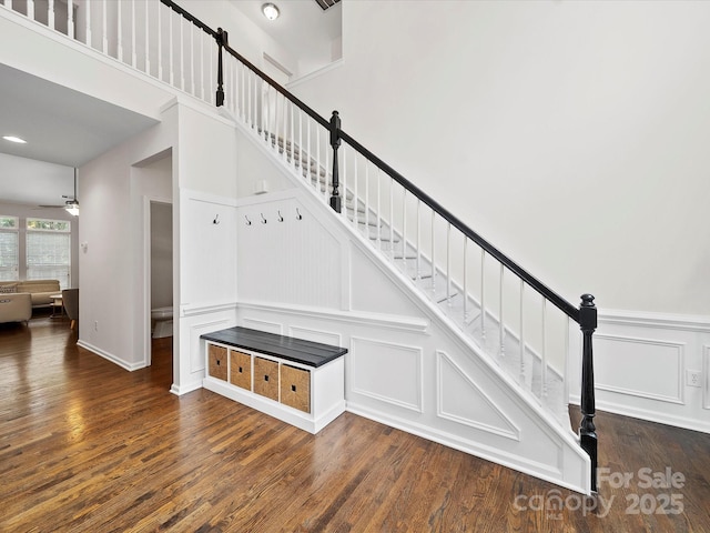 stairs featuring wood finished floors, a decorative wall, a ceiling fan, and a wainscoted wall