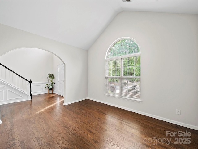 unfurnished living room with stairway, arched walkways, wood finished floors, and lofted ceiling