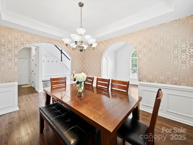 dining space with arched walkways, an inviting chandelier, wallpapered walls, a wainscoted wall, and dark wood-type flooring