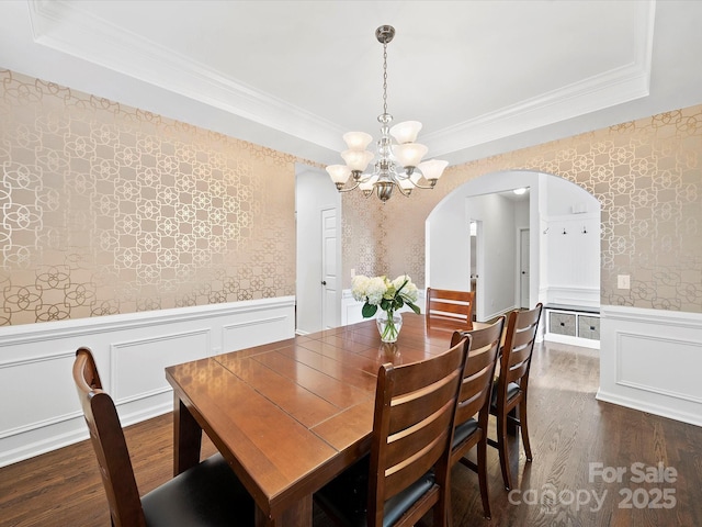 dining area with a notable chandelier, crown molding, arched walkways, wainscoting, and dark wood finished floors