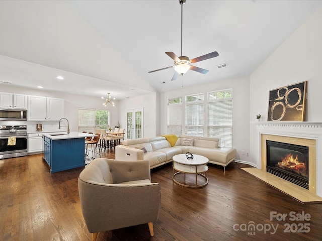 living area with ceiling fan with notable chandelier, a premium fireplace, dark wood-style floors, visible vents, and high vaulted ceiling