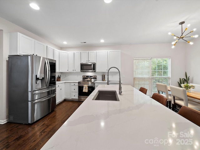 kitchen featuring light stone counters, white cabinetry, a sink, appliances with stainless steel finishes, and dark wood-style floors