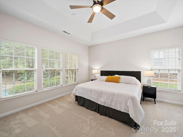 carpeted bedroom with visible vents, multiple windows, a raised ceiling, and baseboards