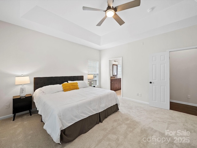 bedroom with baseboards, ensuite bathroom, carpet flooring, and a tray ceiling
